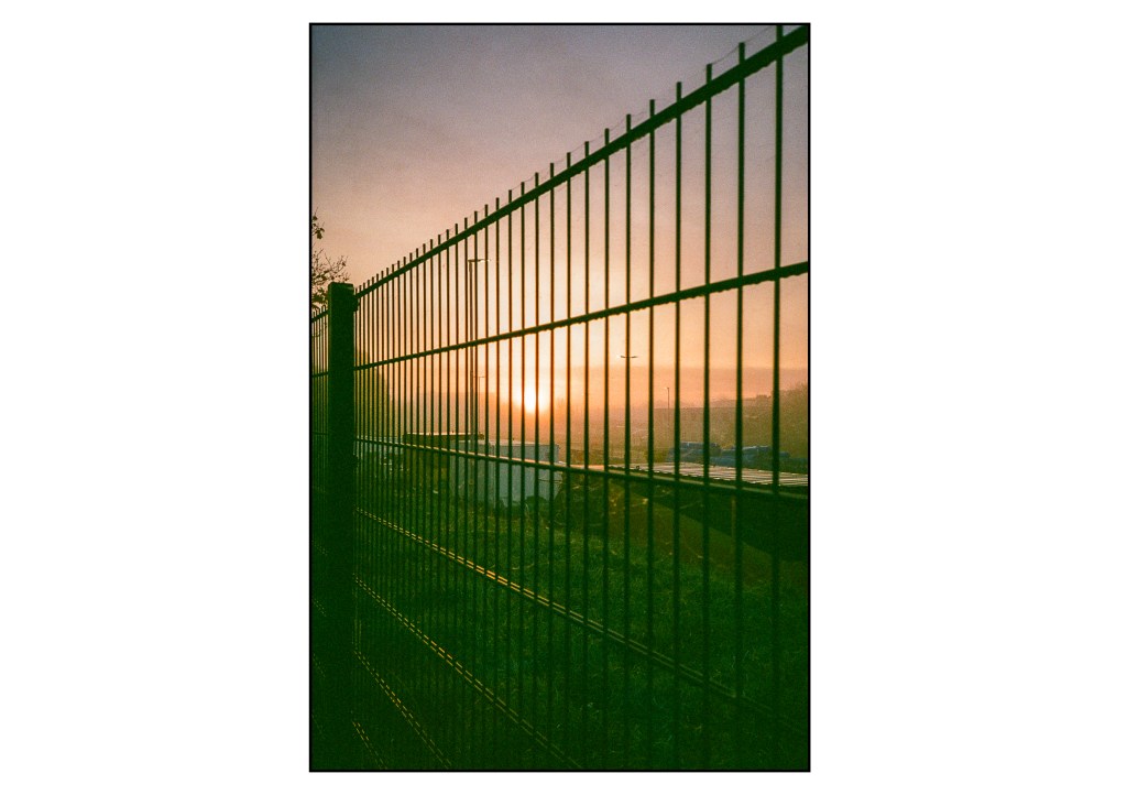 A photo of the sunrise through a fence