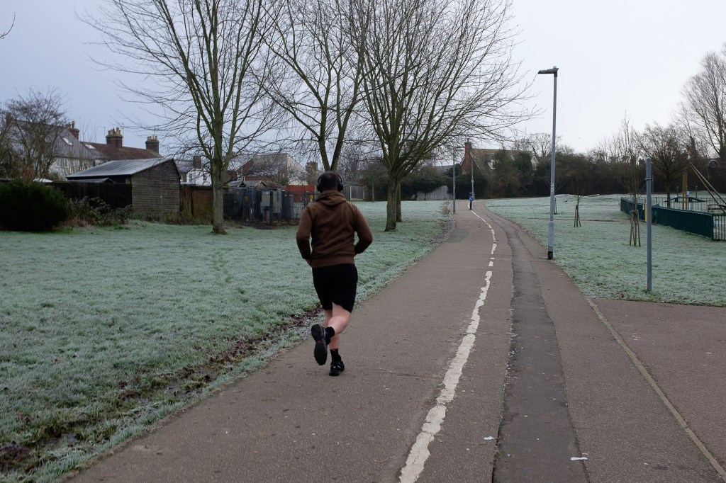 A man in shorts and sweater running in a frosty park