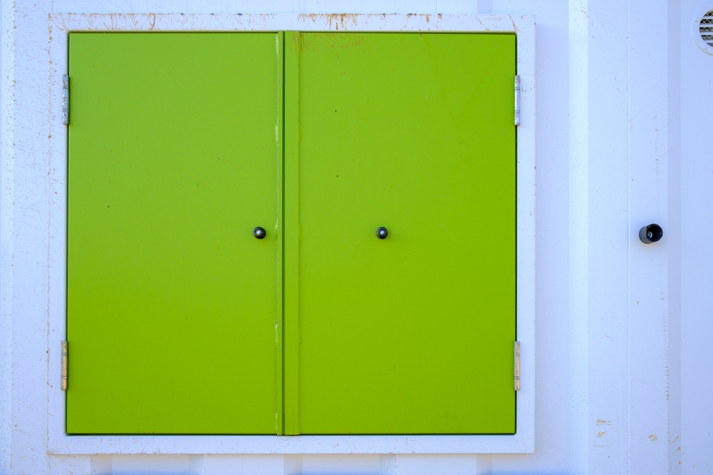 A bright green pair of doors are closed against a white metal hut