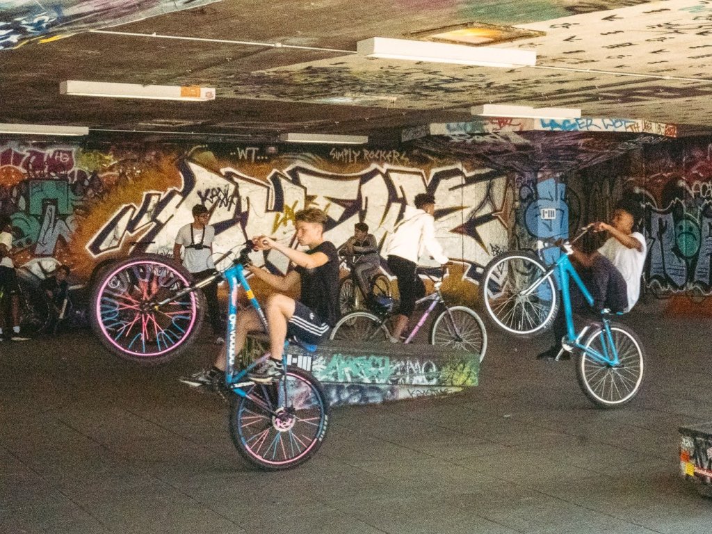 Two young men perform wheelies on mountain bikes in London