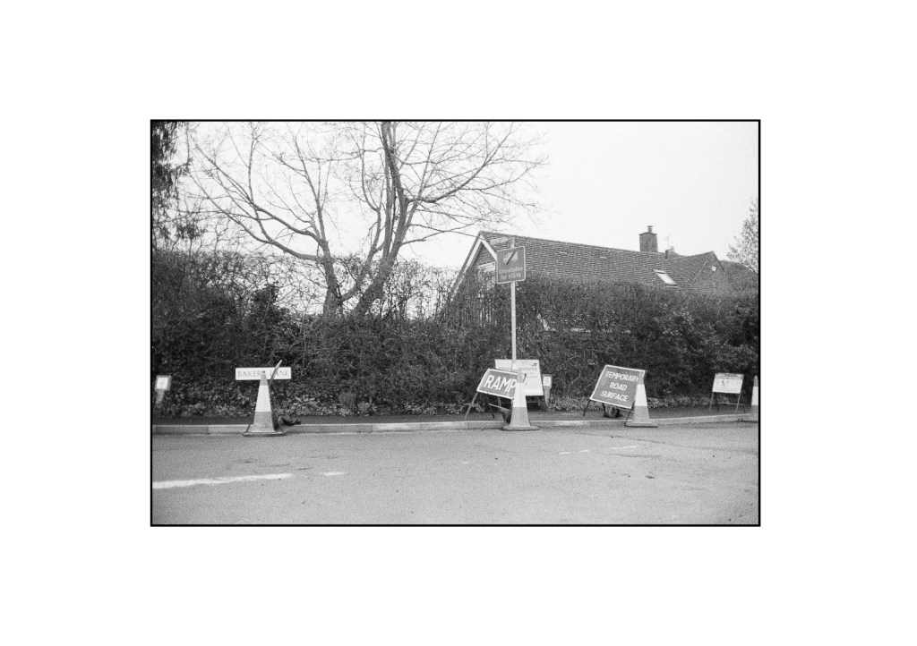 A black and white photo of a collection of various road signs littering a corner in Essex