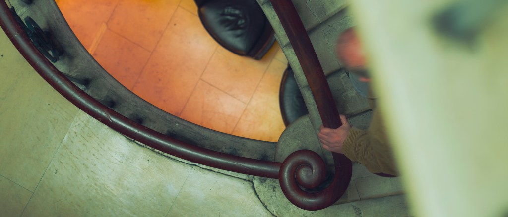 A man grips the hand rail as he walks up a grand marble staircase
