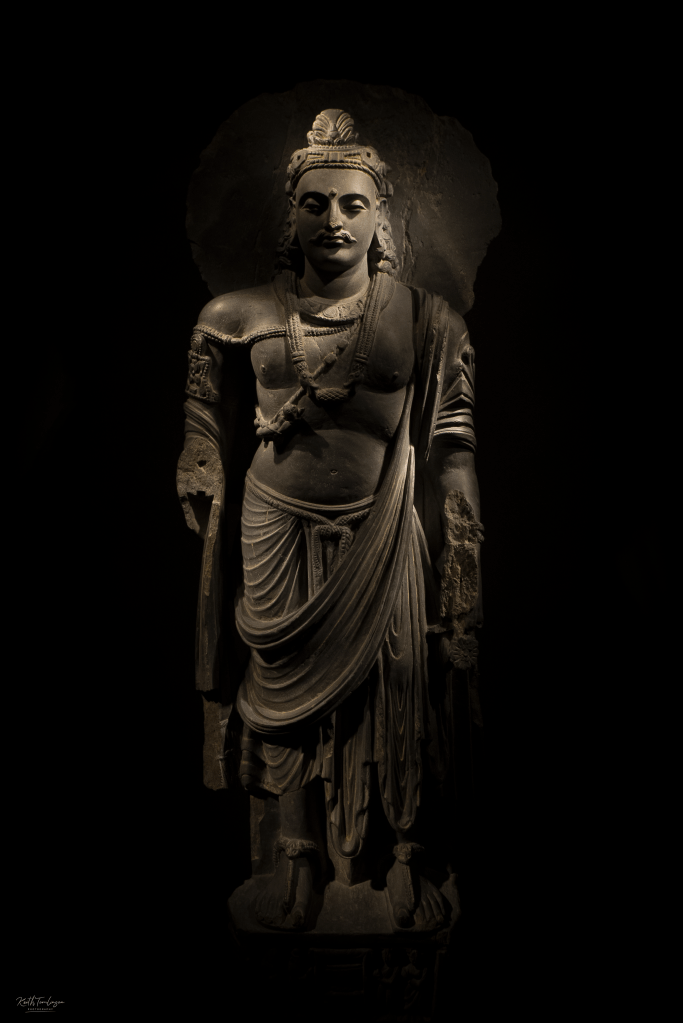A study of an ancient Indian statue which is lit in a dark room with subtle lighting from above